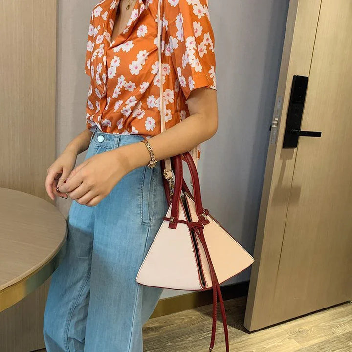 Woman wearing orange floral blouse and light blue jeans carrying beige and burgundy handbag indoors