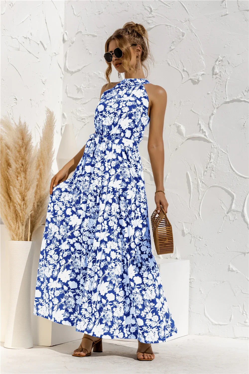 Women wearing blue and white floral halter neck maxi dress with belt holding bamboo handbag