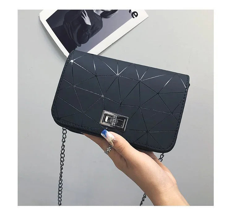 Hand holding a black geometric patterned purse with silver clasp and chain strap on gray background