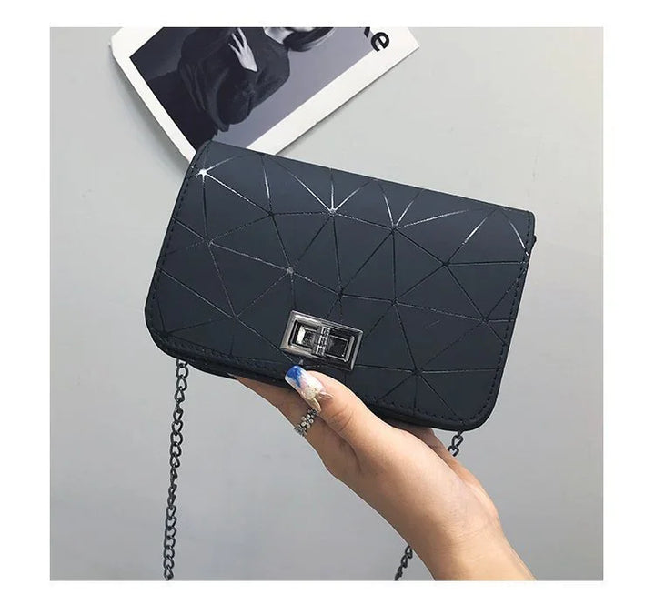 Hand holding a black geometric patterned purse with silver clasp and chain strap on gray background
