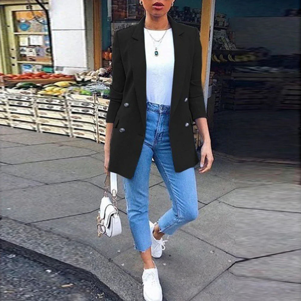 Woman wearing black blazer, white t-shirt, light blue jeans, and white sneakers walking past a produce market