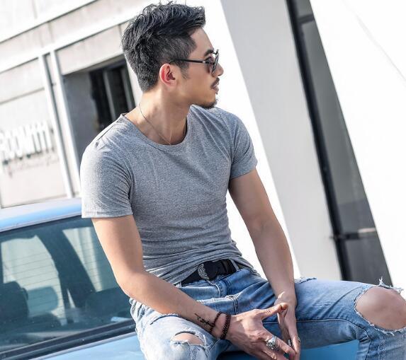Young man in sunglasses wearing a grey t-shirt and ripped jeans sitting on a car outdoors