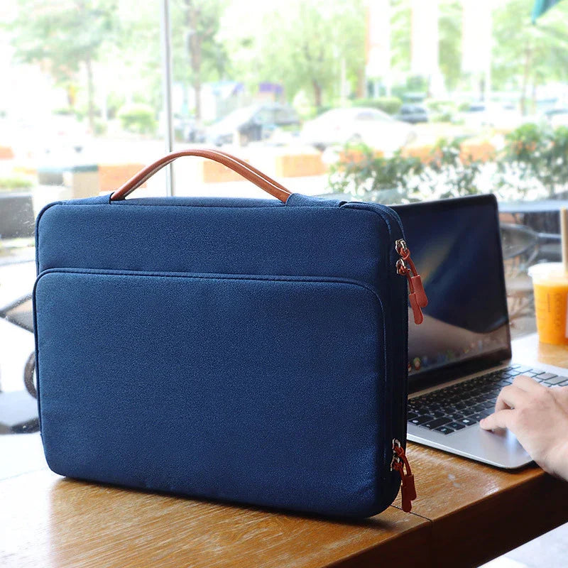 Blue laptop sleeve with brown leather handle on wooden table beside open laptop and iced coffee