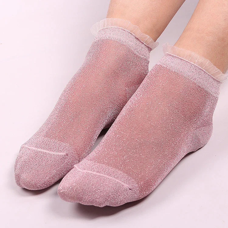Pair of feet wearing sheer pink glitter ankle socks with ruffled cuffs on a light background