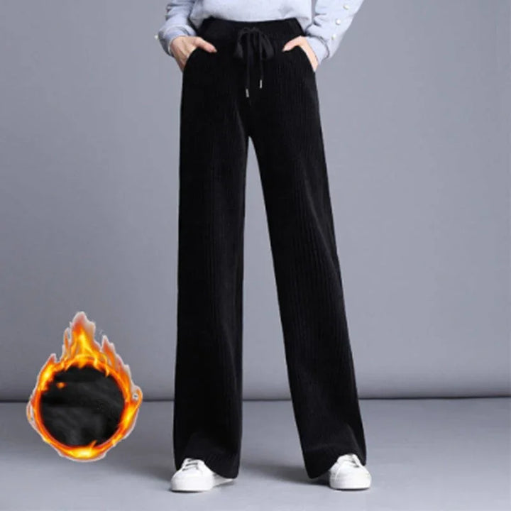 Black wide-leg corduroy pants with drawstring waist worn with white sneakers on gray background