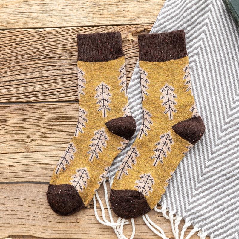 Pair of mustard yellow socks with brown cuffs and toes featuring leaf patterns on wooden surface with gray striped textile
