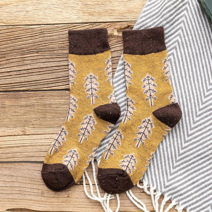 Pair of mustard yellow socks with brown cuffs and toes featuring leaf patterns on wooden surface with gray striped textile