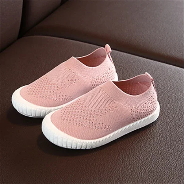 Pair of pink knitted slip-on shoes with white rubber soles on brown surface