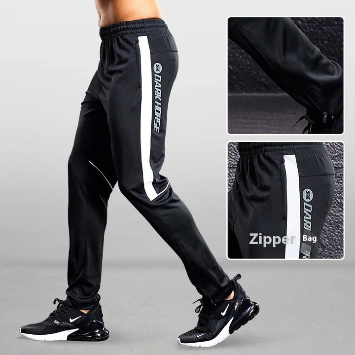 Black athletic joggers with white side stripe and zipper pockets, worn with black Nike sneakers