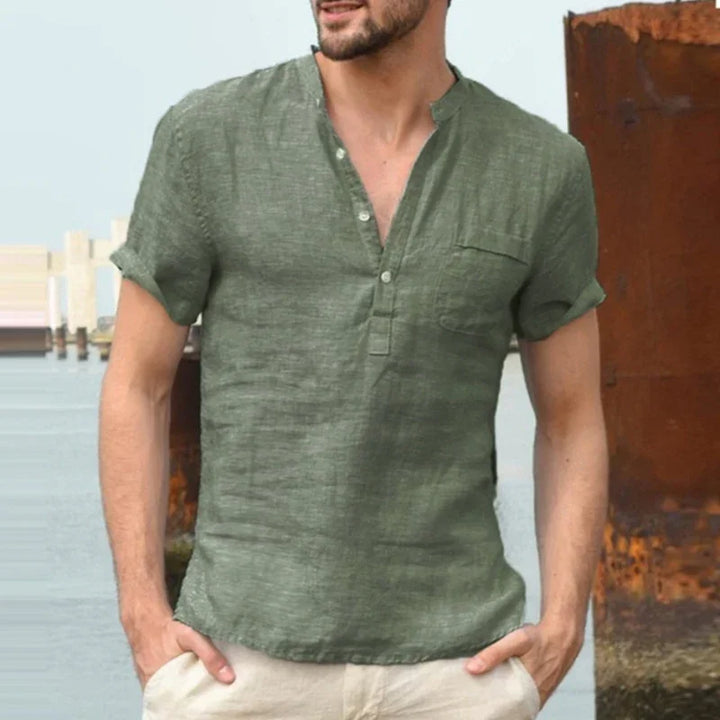 Man wearing casual green short-sleeve linen shirt with half-placket and beige pants by the waterfront