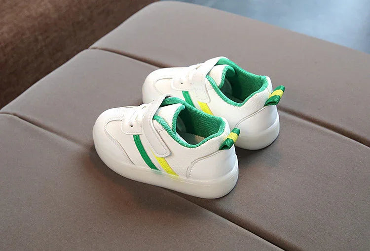 White toddler sneakers with green and yellow stripes, cushioned interior, on brown surface
