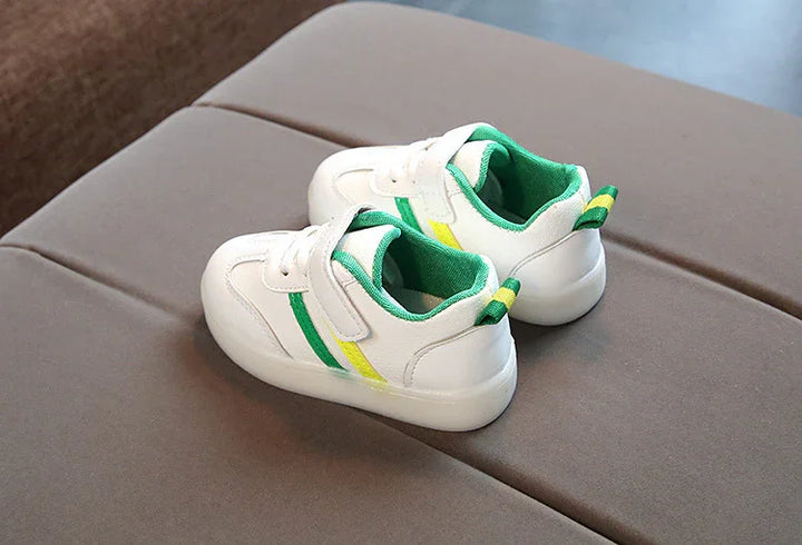 White toddler sneakers with green and yellow stripes, cushioned interior, on brown surface