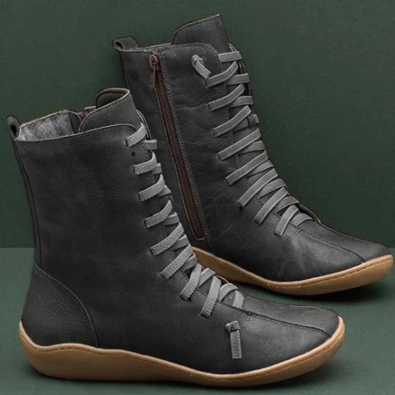 Black leather lace-up ankle boots with brown soles and side zippers on green background