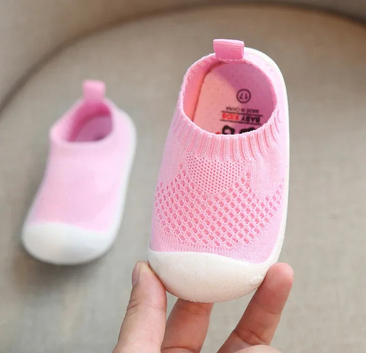 Hand holding pink baby sock shoes with white soles on beige background