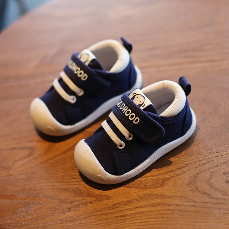 Navy blue baby shoes with white soles and laces, labeled 'Childhood,' on wooden surface