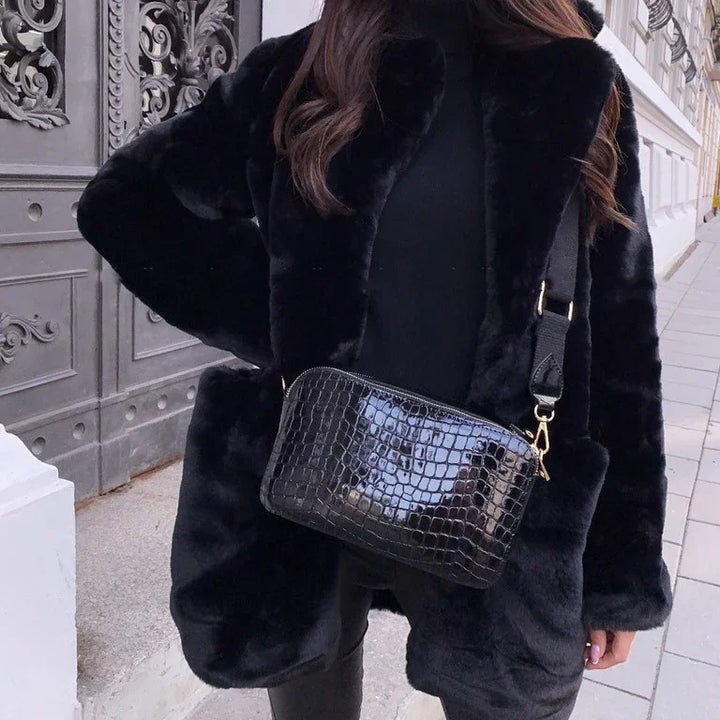 Woman wearing black faux fur coat and black crocodile leather crossbody bag on city sidewalk