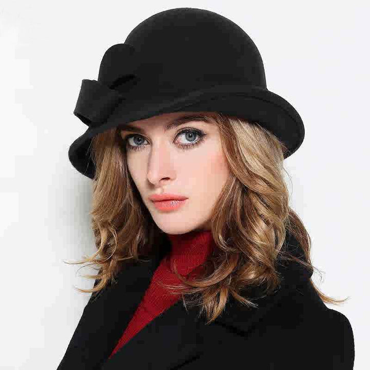 Woman wearing a black cloche hat with bow, black coat, and red turtleneck against white background