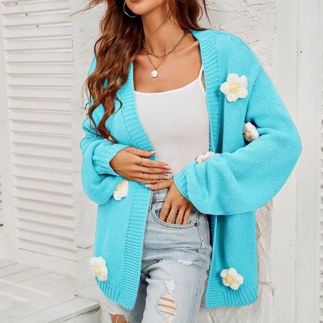 Woman wearing light blue knitted cardigan with white flower appliques over white tank and distressed denim shorts
