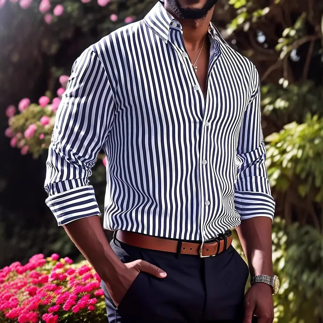 Man wearing a navy and white vertical striped shirt, brown belt, and navy pants in garden setting