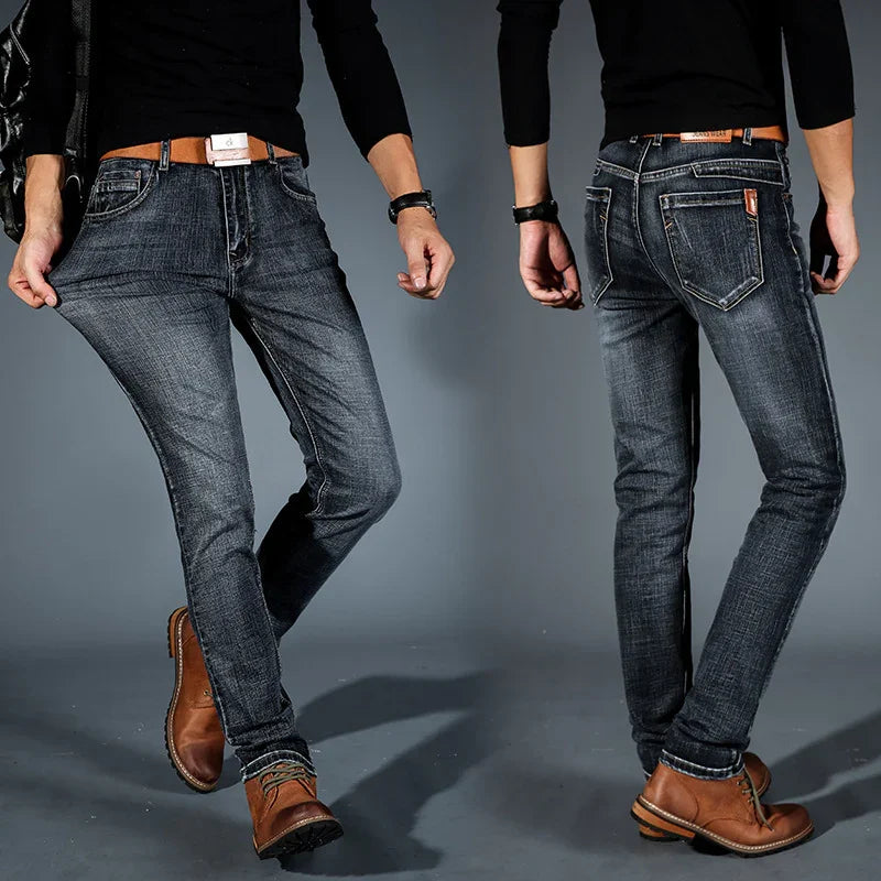 Men's slim fit dark wash jeans paired with brown leather boots on a gray background