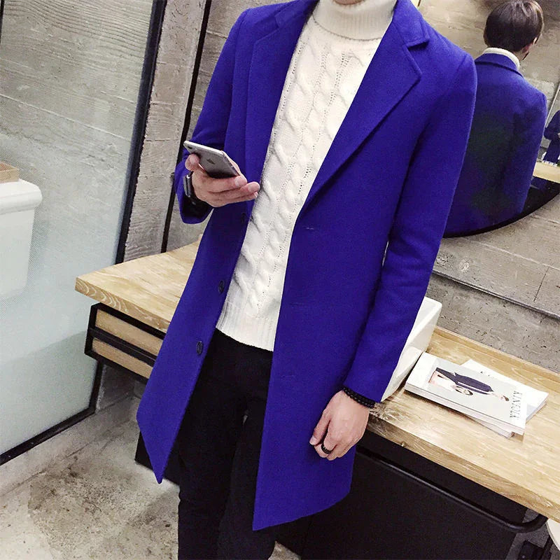 Man wearing royal blue overcoat and white cable knit turtleneck sweater holding a smartphone indoors