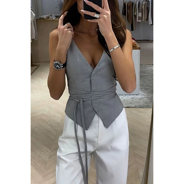 Woman wearing gray wrap waist vest with deep V-neck and white high-waisted pants in modern boutique
