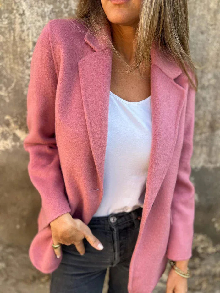 Woman wearing a pink wool coat over a white top and black jeans against a textured wall background