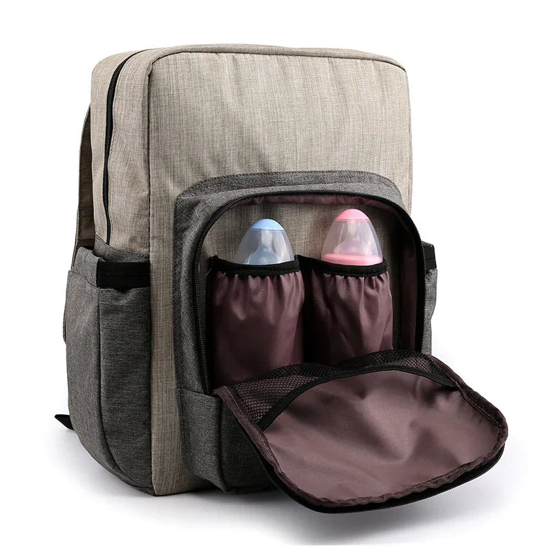 Beige and gray backpack with front pocket holding two baby bottles with blue and pink lids