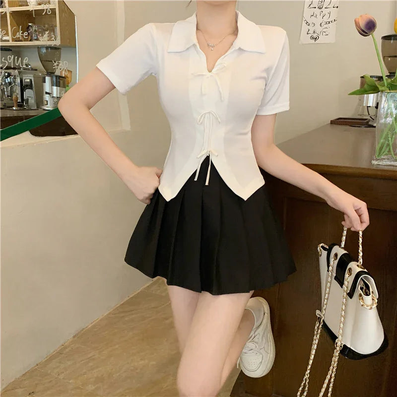 Woman wearing white short-sleeve top and black pleated skirt holding white handbag with gold chain in cafe