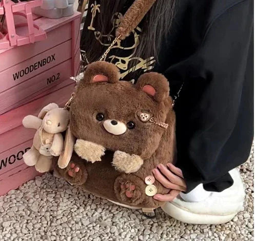 person holding plush bear-shaped handbag with a small bunny keychain next to pink wooden boxes