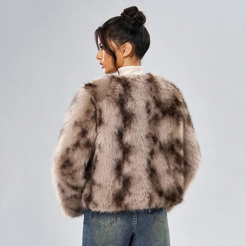 Woman wearing a brown patterned faux fur jacket and blue jeans, posing against gray background