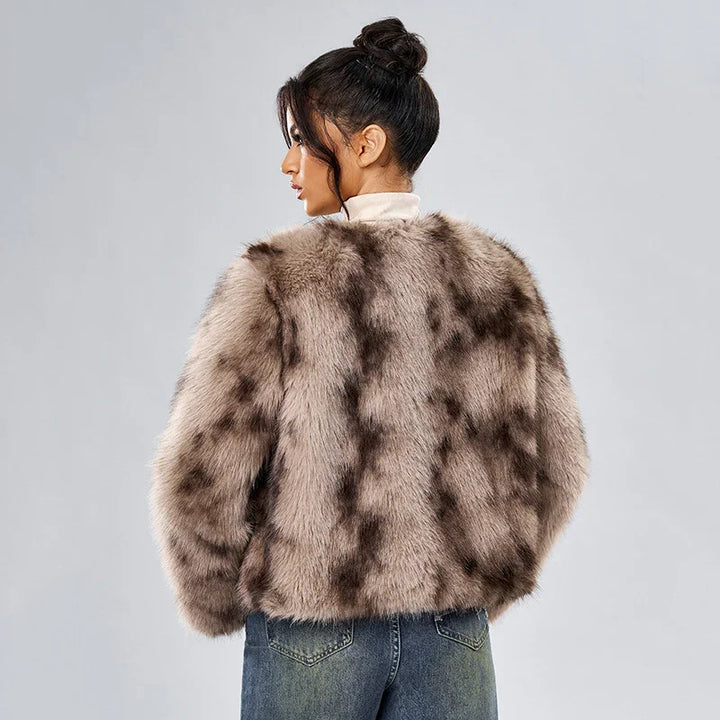 Woman wearing a brown patterned faux fur jacket and blue jeans, posing against gray background