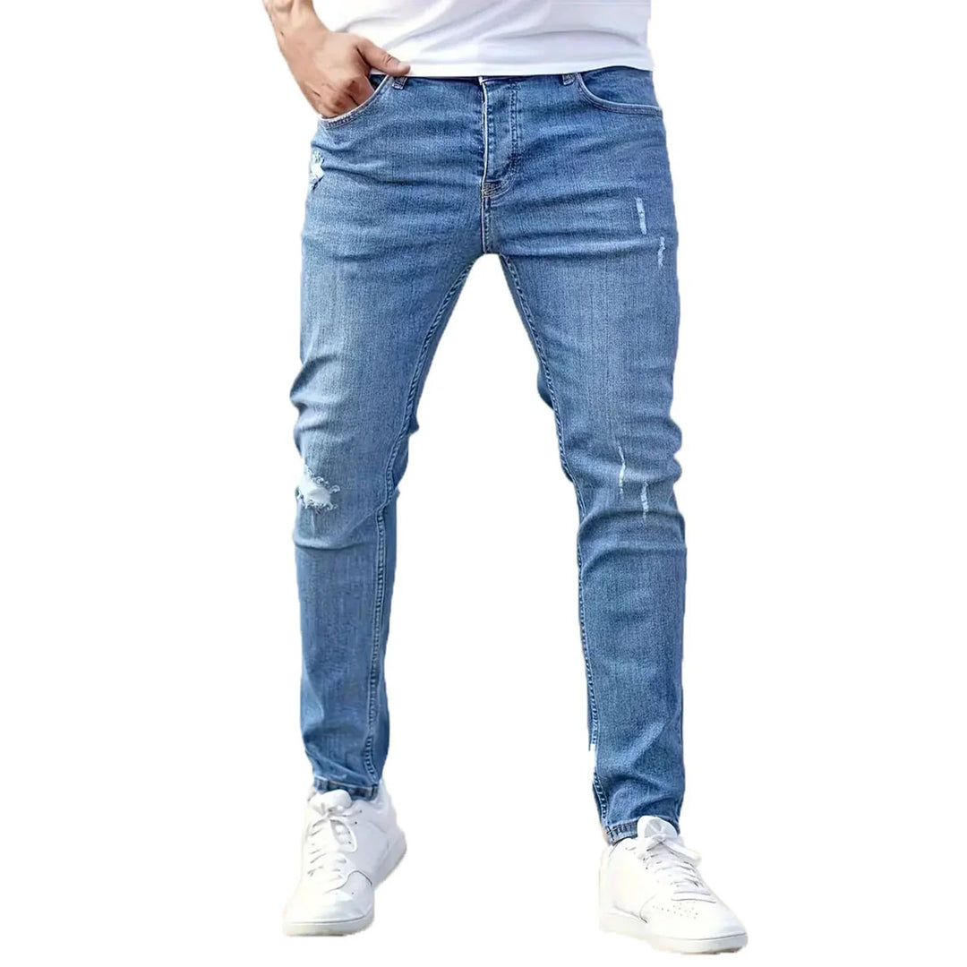 Man wearing slim fit distressed blue jeans and white sneakers on white background