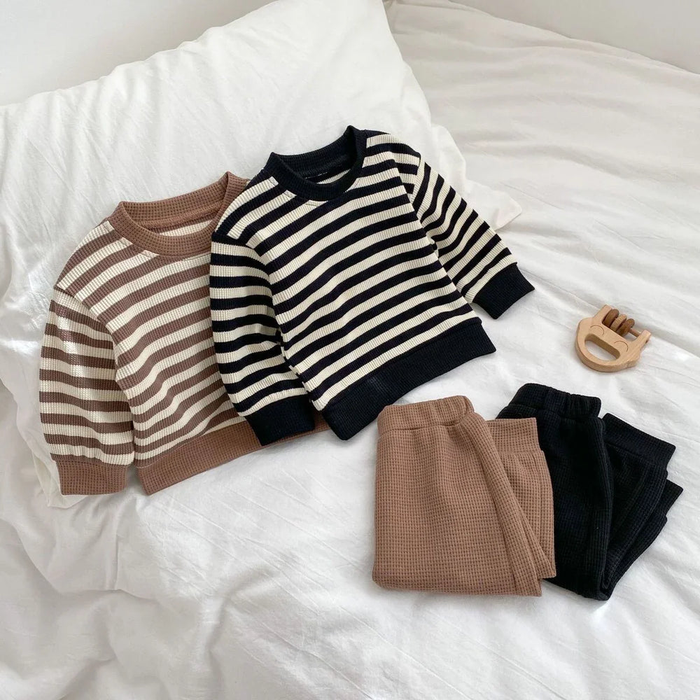 Two striped knit sweaters in brown and black with matching waffle knit pants on white bed