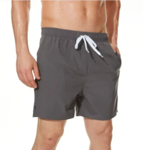 Man wearing dark gray swim shorts with white drawstring, standing with hands in pockets
