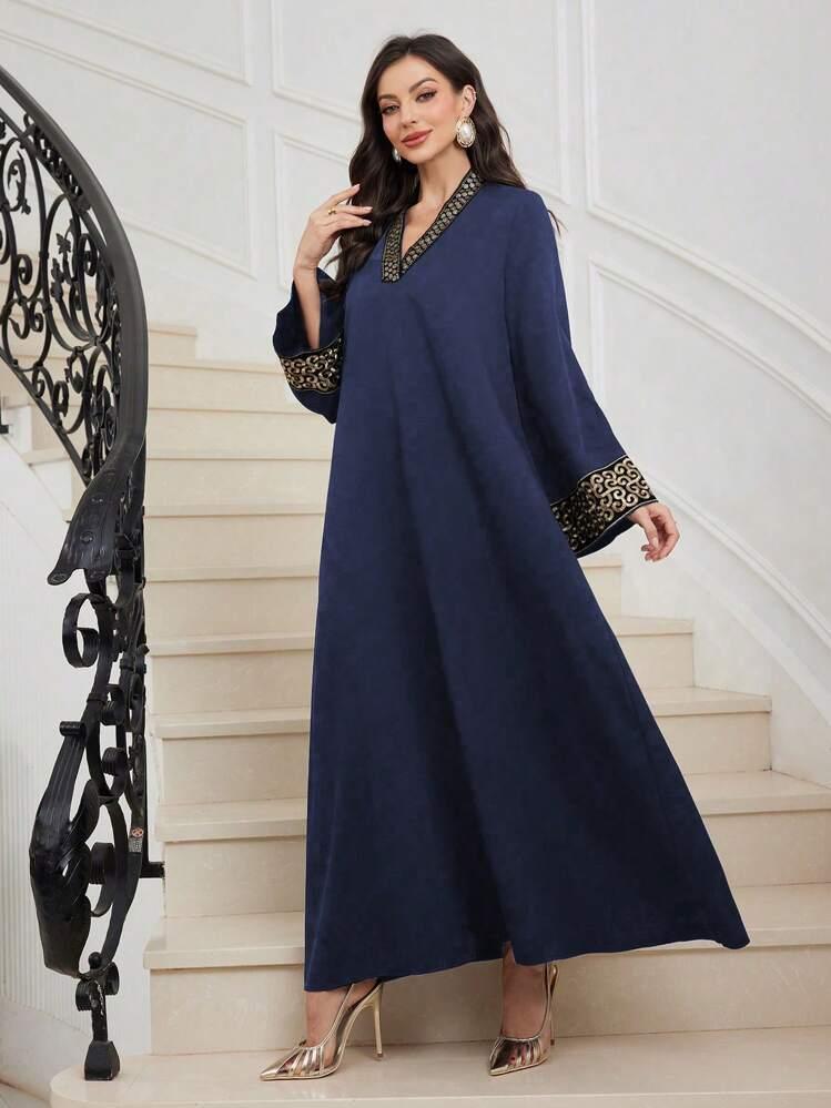 Woman wearing a navy blue abaya with gold embroidered cuffs and neckline, standing on staircase