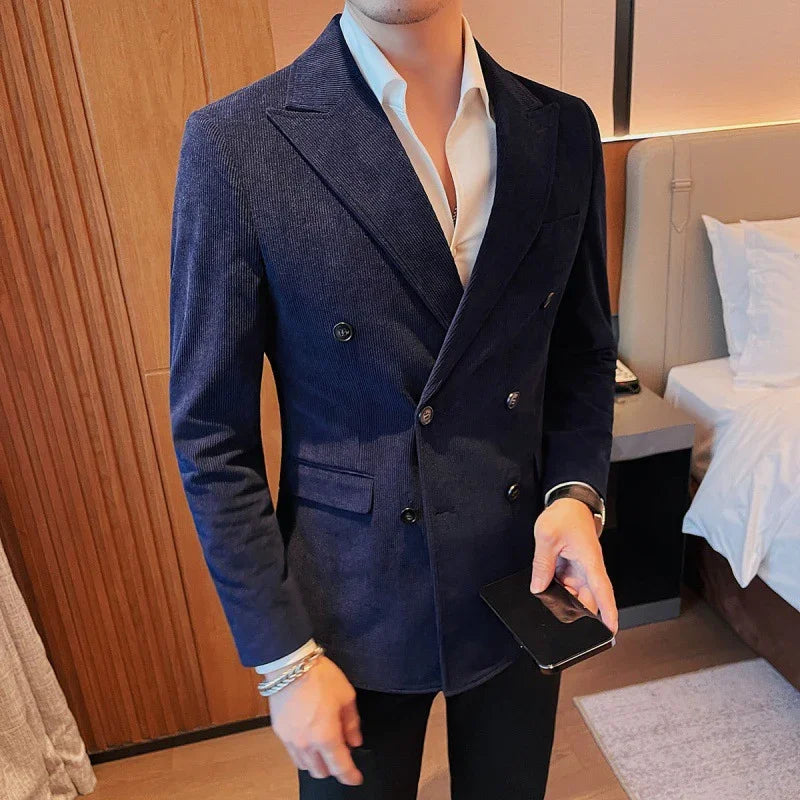 Man wearing navy double-breasted blazer with white shirt, holding black smartphone indoors