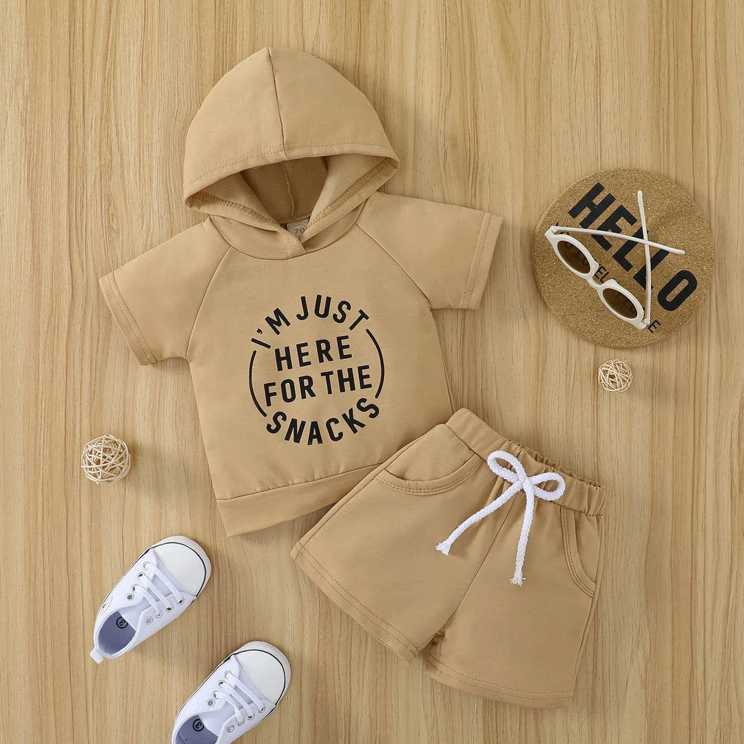 Beige toddler hoodie and shorts set with "I'm just here for the snacks" text, paired with white shoes and sunglasses