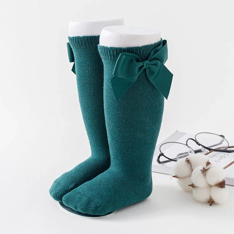 Teal knee-high knit socks with decorative bows on white mannequins, displayed with cotton and glasses