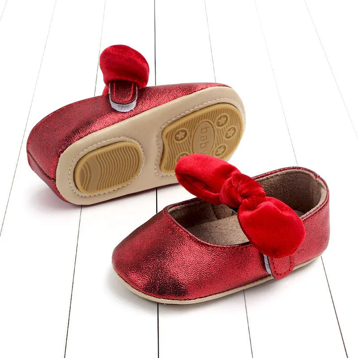 Red baby girl shoes with soft suede soles and velvet bow on white wooden floor