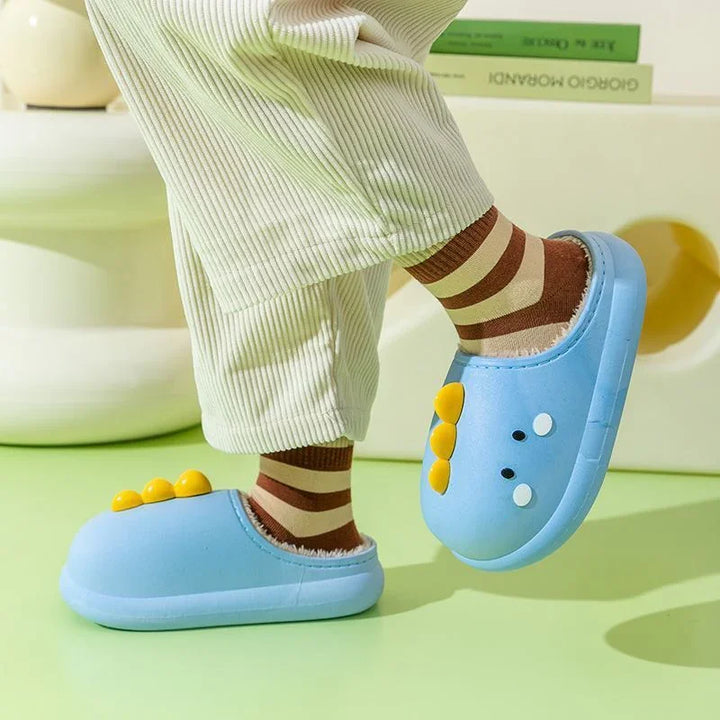 Child wearing blue dinosaur slippers with yellow spikes and brown striped socks indoors