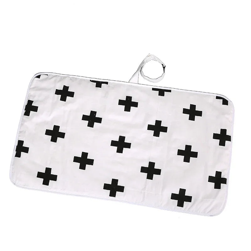 White baby changing mat with black cross pattern and attached strap