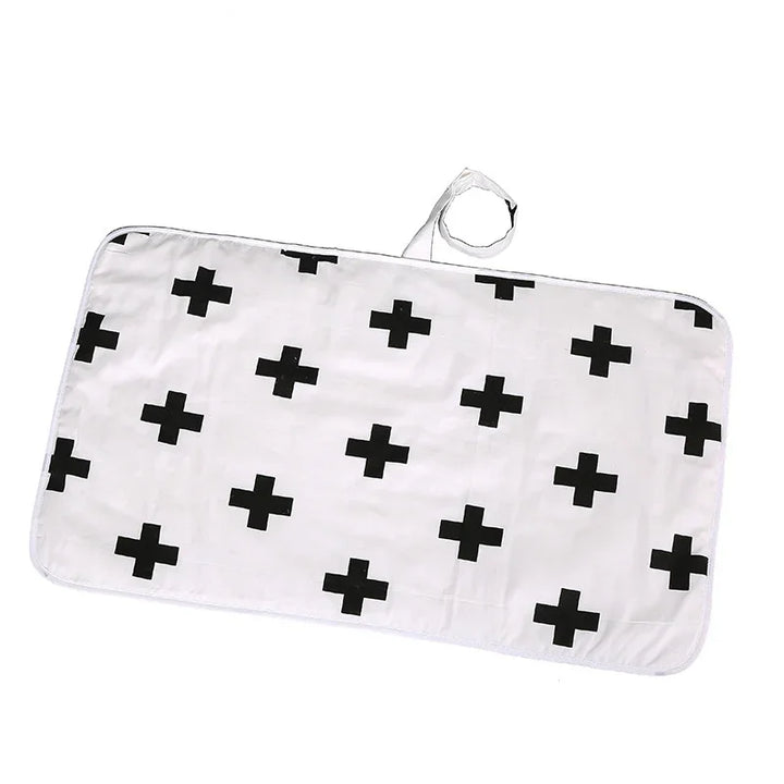 White baby changing mat with black cross pattern and attached strap