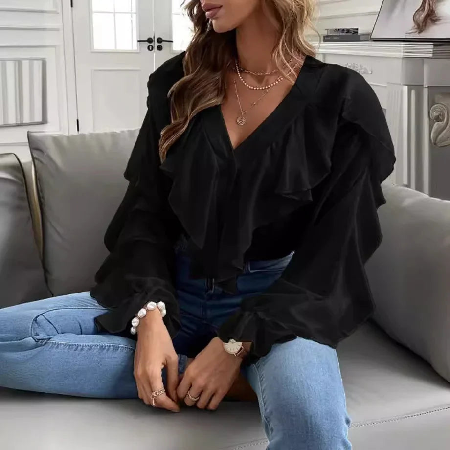 Woman wearing black ruffled blouse and light blue jeans seated on gray sofa in stylish room