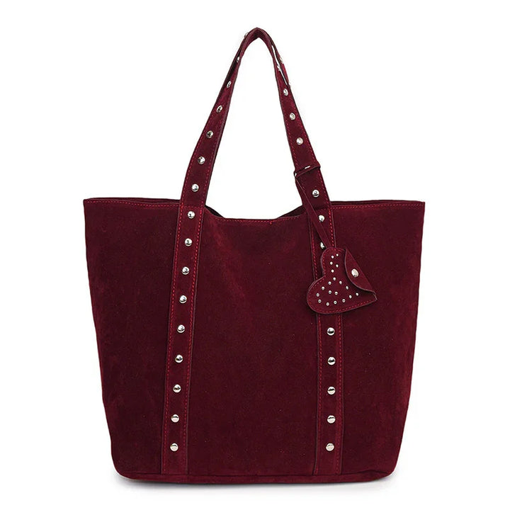 Burgundy suede tote bag with silver studs and heart-shaped charm on white background