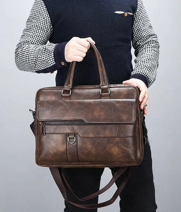 Brown leather briefcase with multiple compartments held by a person in checkered shirt and black vest