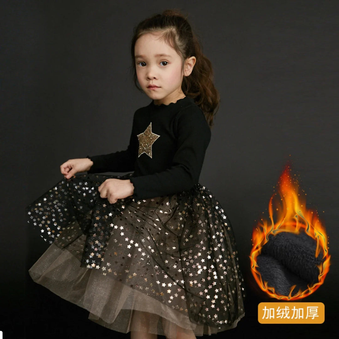 Little girl wearing black long sleeve dress with gold star and star-patterned tulle skirt on dark background