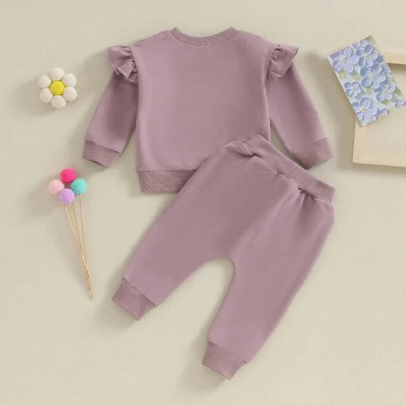 Soft mauve toddler outfit with ruffled long sleeves and matching pants on beige background