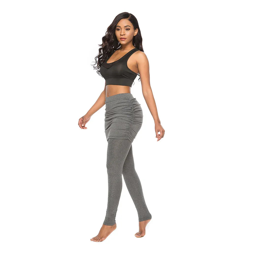 Woman wearing black sports bra and ruched grey leggings, posing barefoot on white background