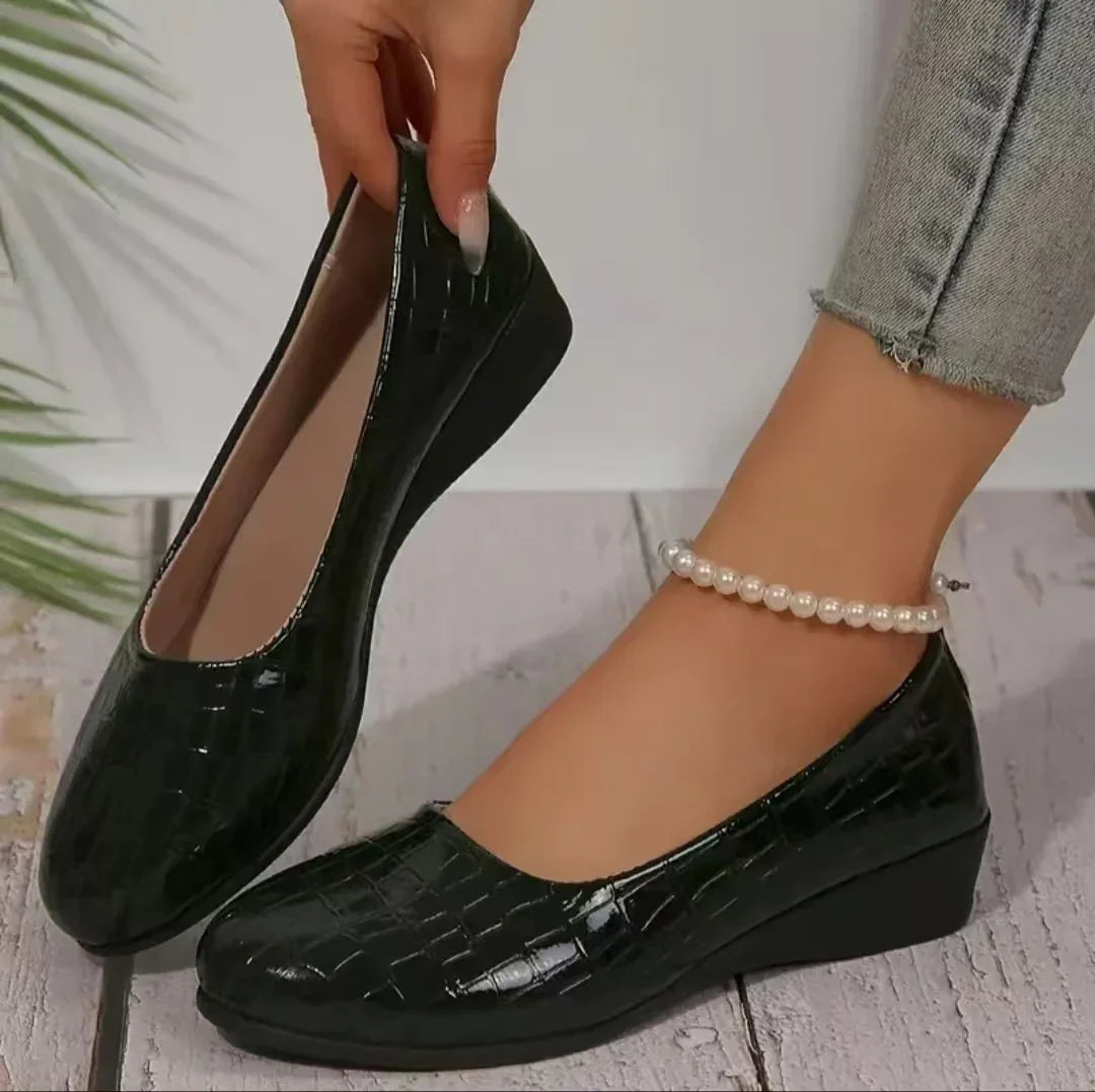 Black crocodile-patterned wedge shoes worn with a pearl anklet and cropped jeans on wooden floor